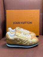 Gold monogram sneakers with white laces and blue-trim rubber sole, side view