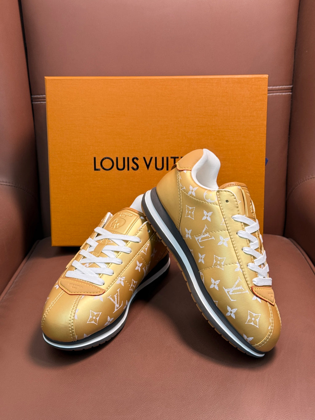 Gold monogram sneakers with white laces, angled pair view, blue-trim soles