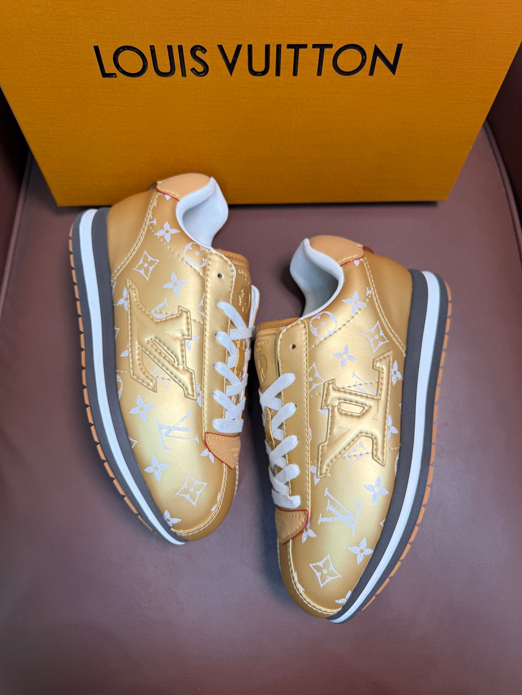 Gold monogram low-top sneakers with white laces, two-quarter view, blue-trim soles