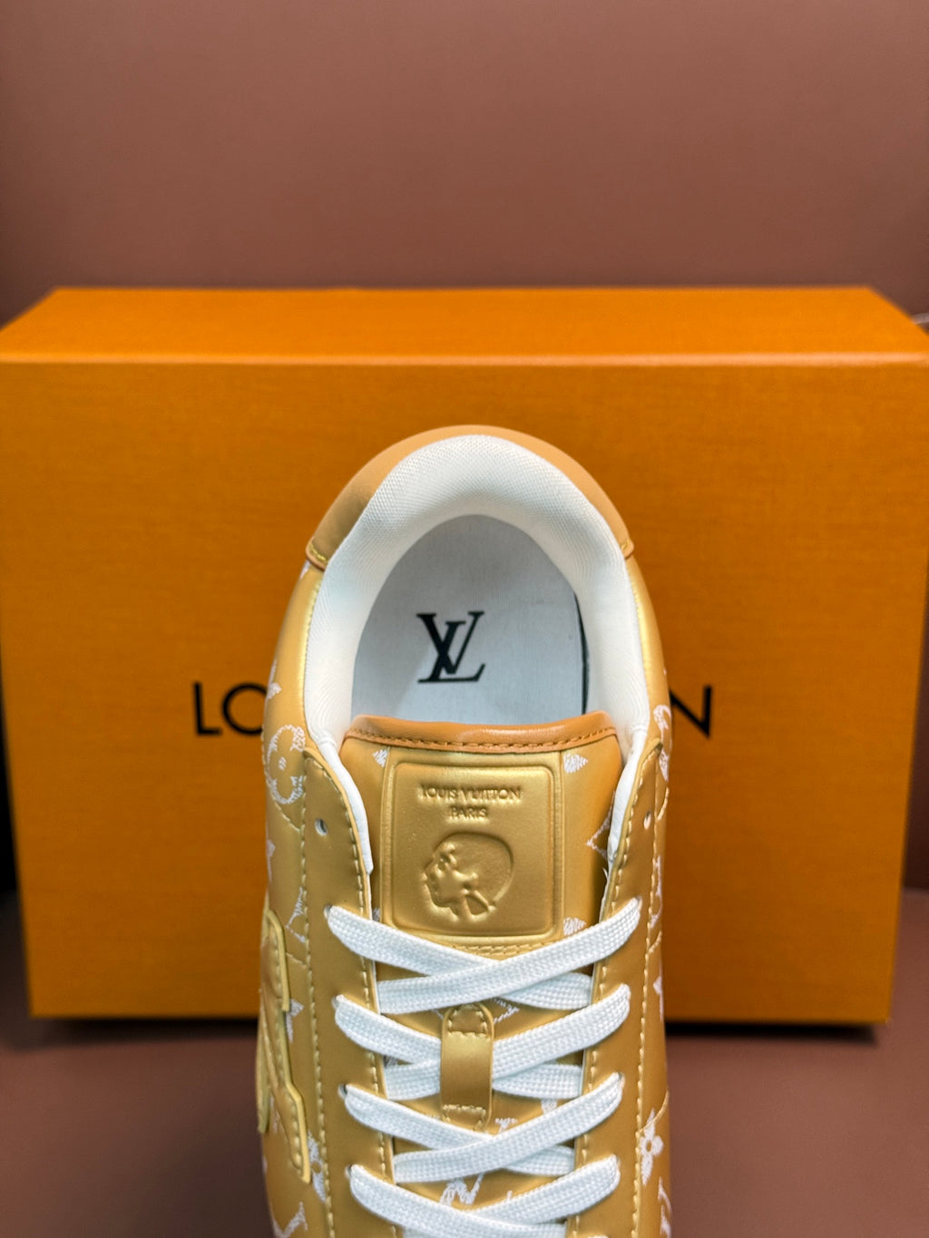 Gold monogram sneaker showing tongue logo and white laces, front upper view