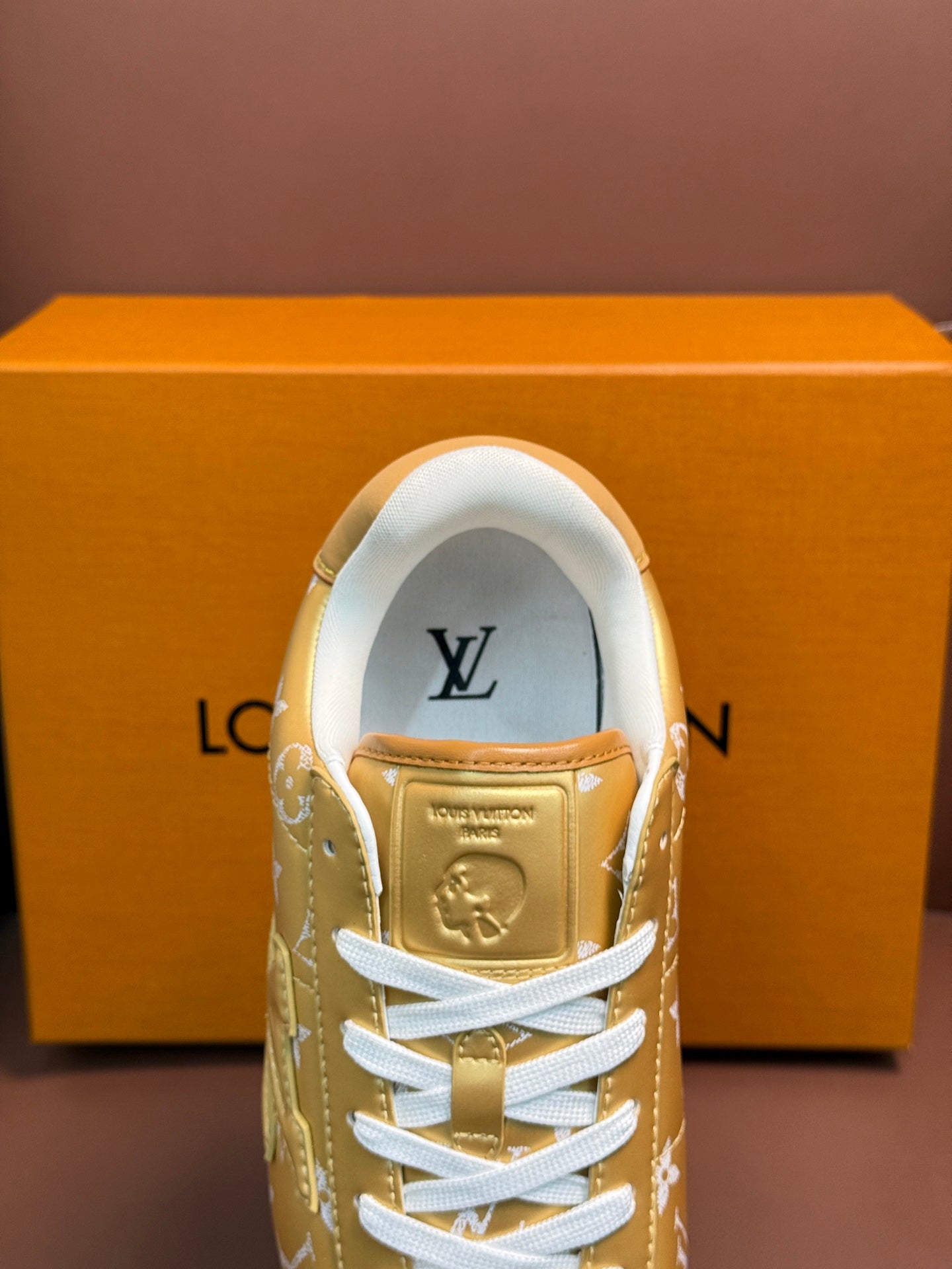 Gold monogram sneaker showing tongue logo and white laces, front upper view