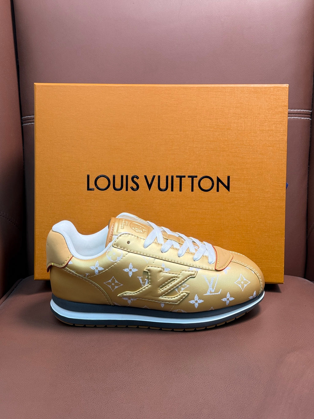 Gold monogram low-top sneakers with white laces and blue-trim sole, angled view