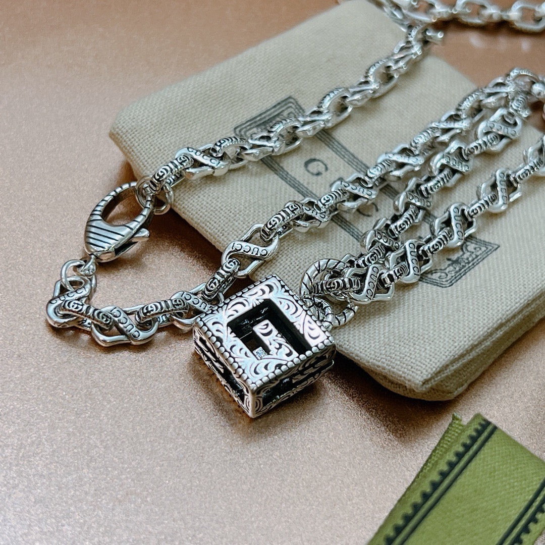 Silver charm necklace with ornate square pendant and figure motif