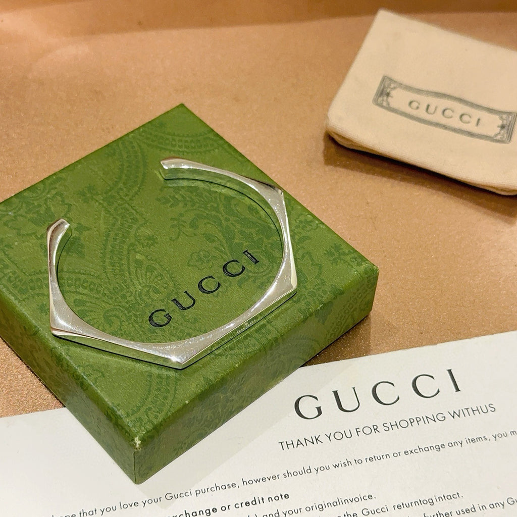 Gucci silver bangle bracelet with hinged cuff and Gucci logo, shown in green box