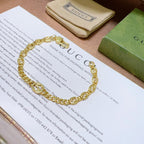 Gold chain bracelet with round links and clasp, on a card and pouch.
