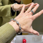 Silver logo-link bracelet worn on wrist with ring