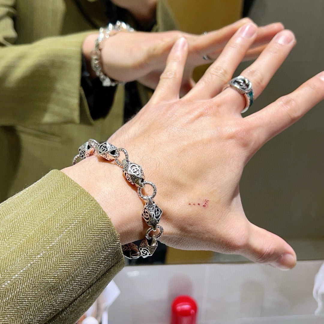 Silver logo-link bracelet worn on wrist with ring