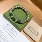 Green and silver charm bracelet on a green box with a fabric pouch