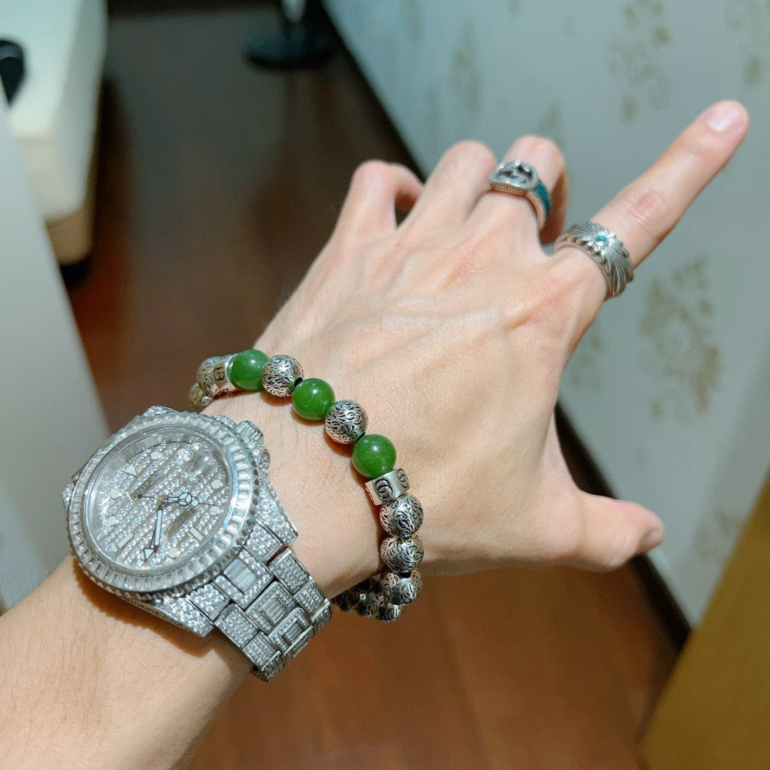 Green beaded silver charm bracelet on wrist, with silver watch visible