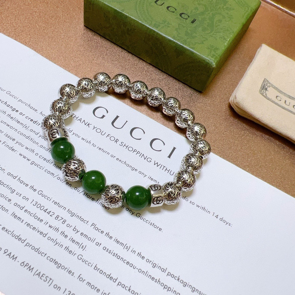 Silver charm bracelet with green beads laid flat on packaging card