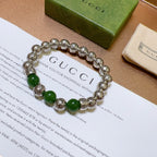 Silver charm bracelet with green beads laid flat on packaging card
