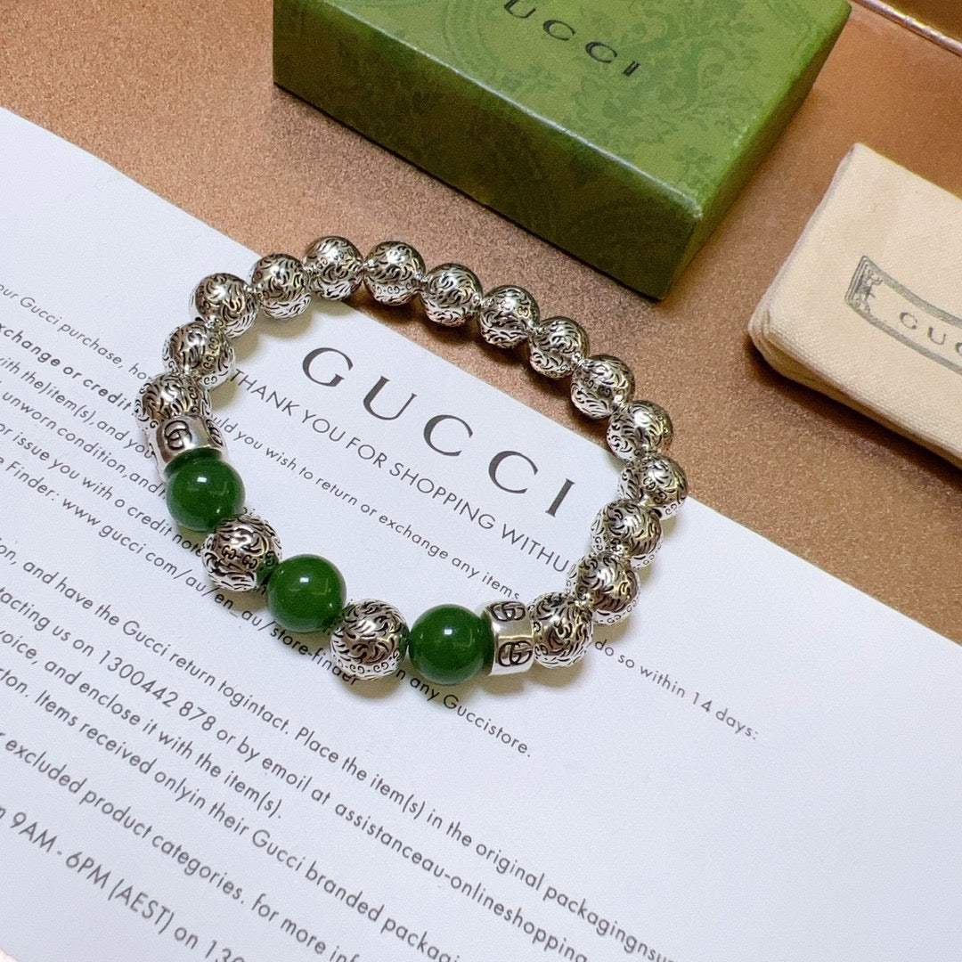 Silver charm bracelet with green beads laid flat on packaging card