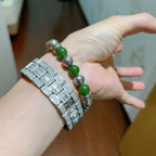 Silver charm bracelet with green beads on wrist, hand resting