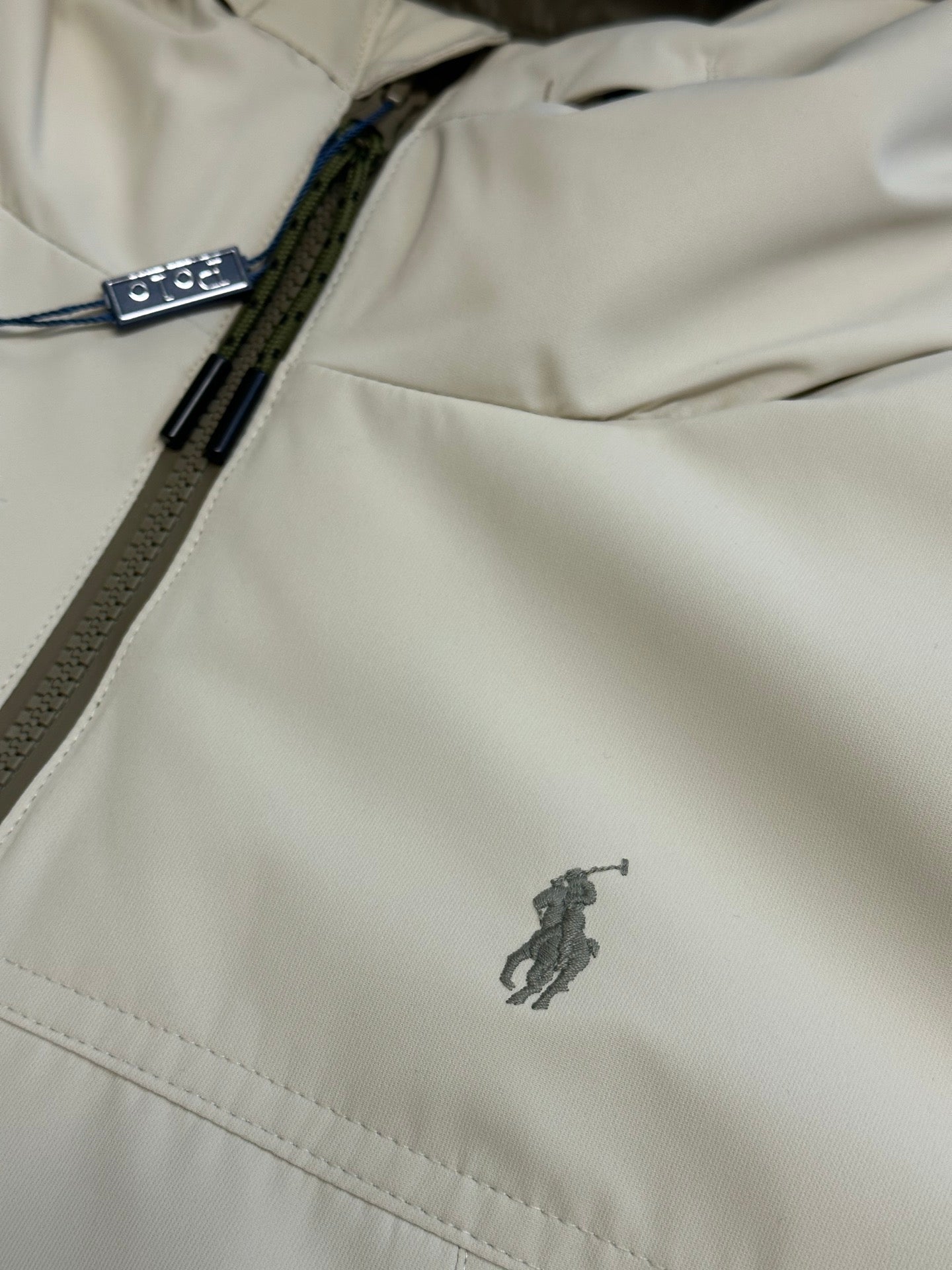 Light beige jacket close-up with side zipper and small embroidered logo