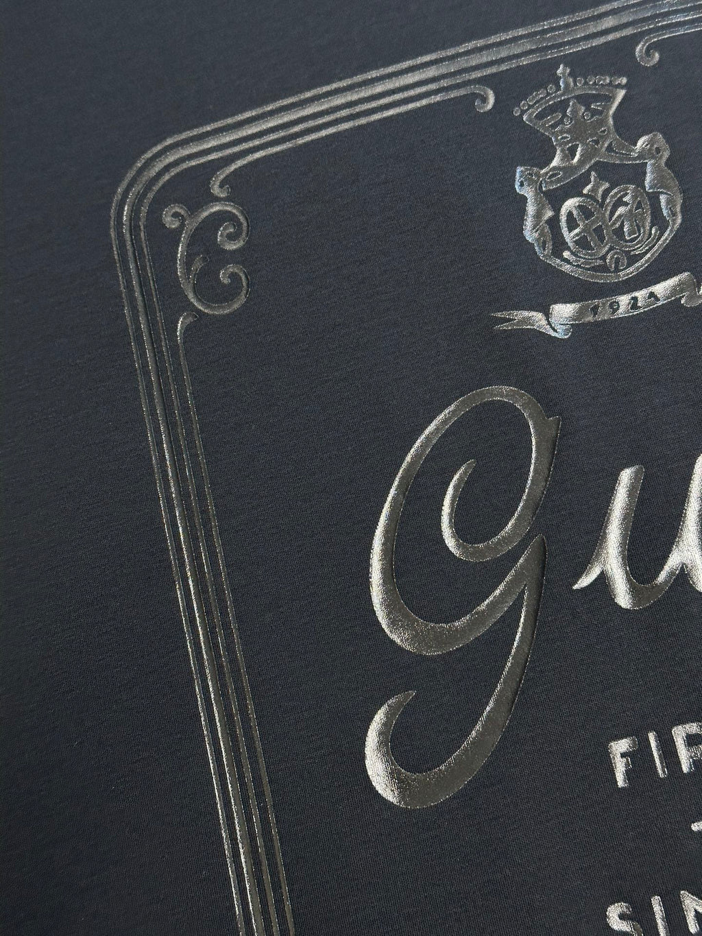 Dark navy T-shirt close-up of metallic crest and Gucci logo print