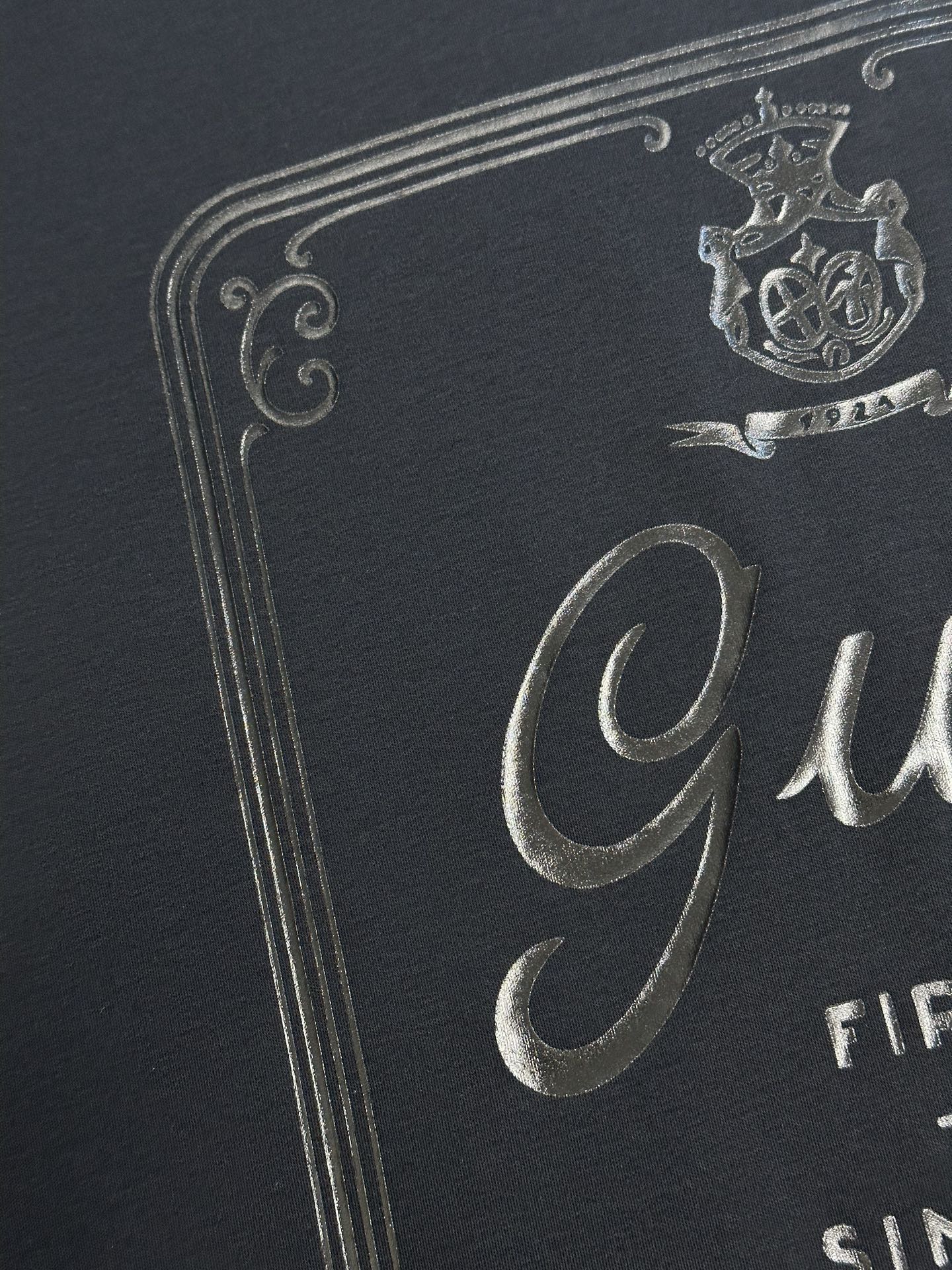 Dark navy T-shirt close-up of metallic crest and Gucci logo print