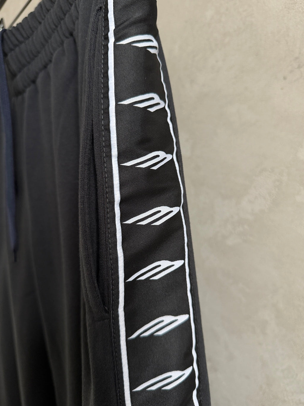 Black track-style pants with elastic waist and white logo stripe along the side