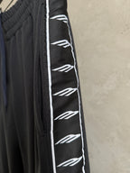 Black track-style pants with elastic waist and white logo stripe along the side