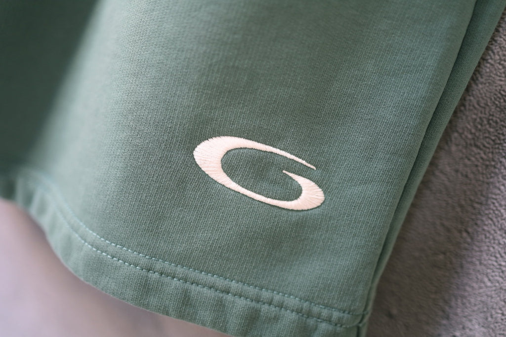 Teal shorts with curved logo patch near the hem