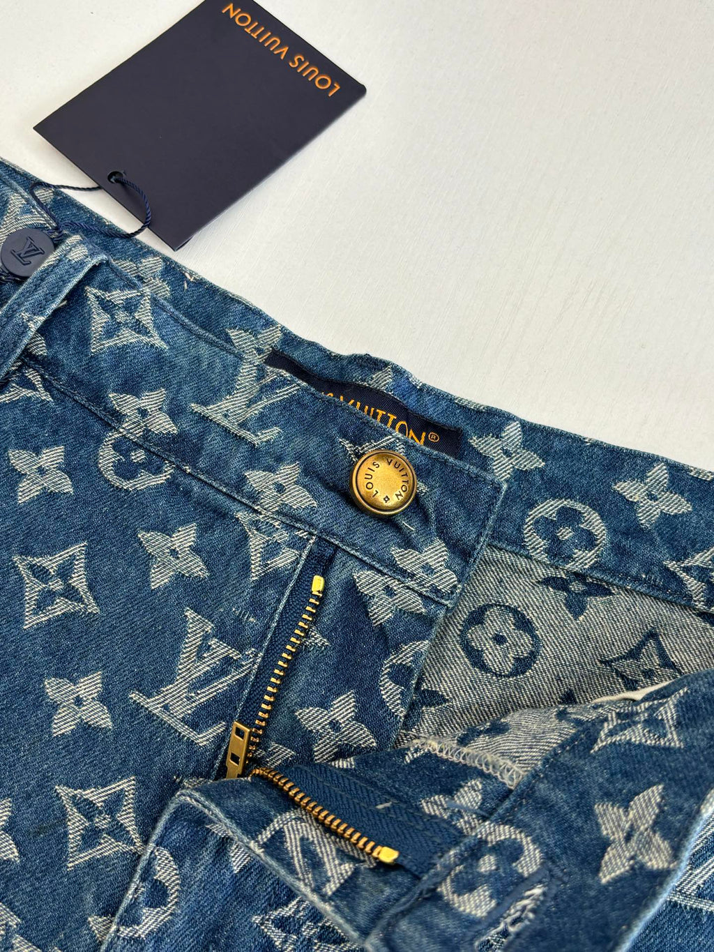 Louis Vuitton blue monogram denim shorts detail, gold button and zip at pocket opening.