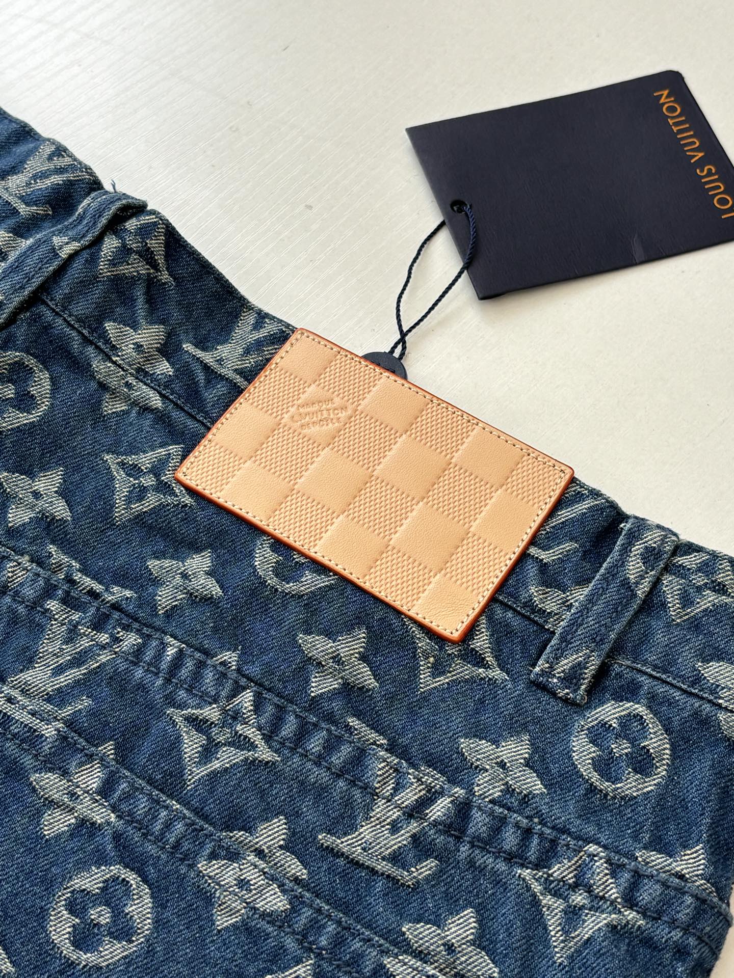 Louis Vuitton blue monogram denim shorts detail with tan leather tag and button placket.