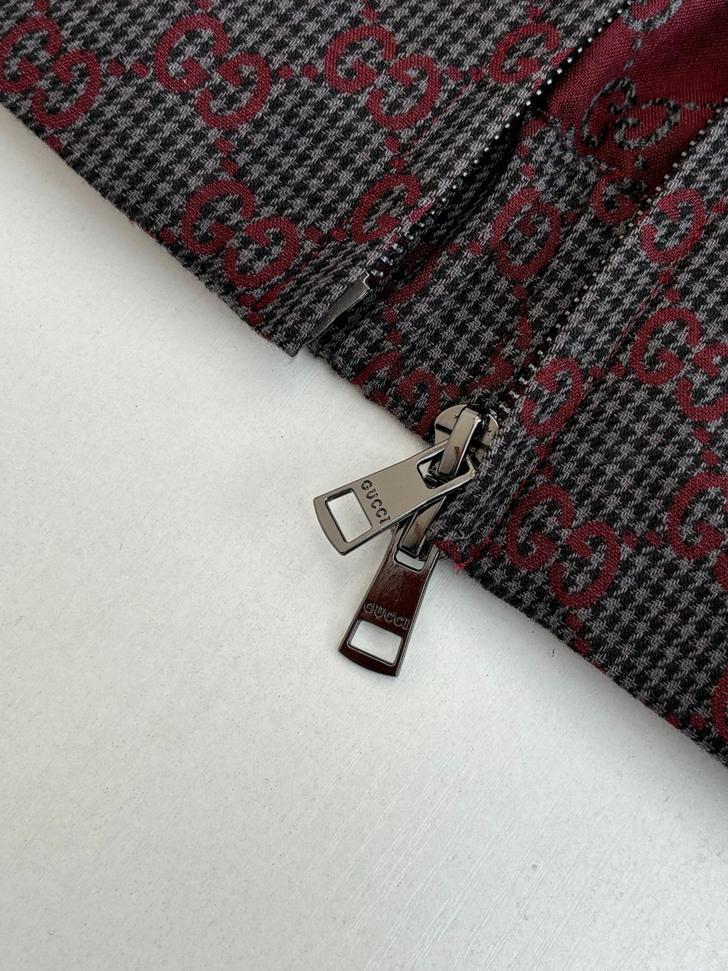 Gucci metal zipper pull on patterned jacket fabric, maroon and dark allover motif.
