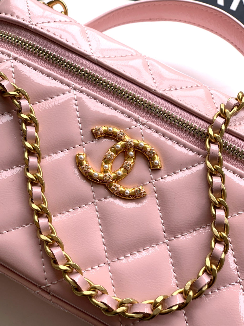 Light pink quilted leather bag close-up of gold-tone CC logo and zipper