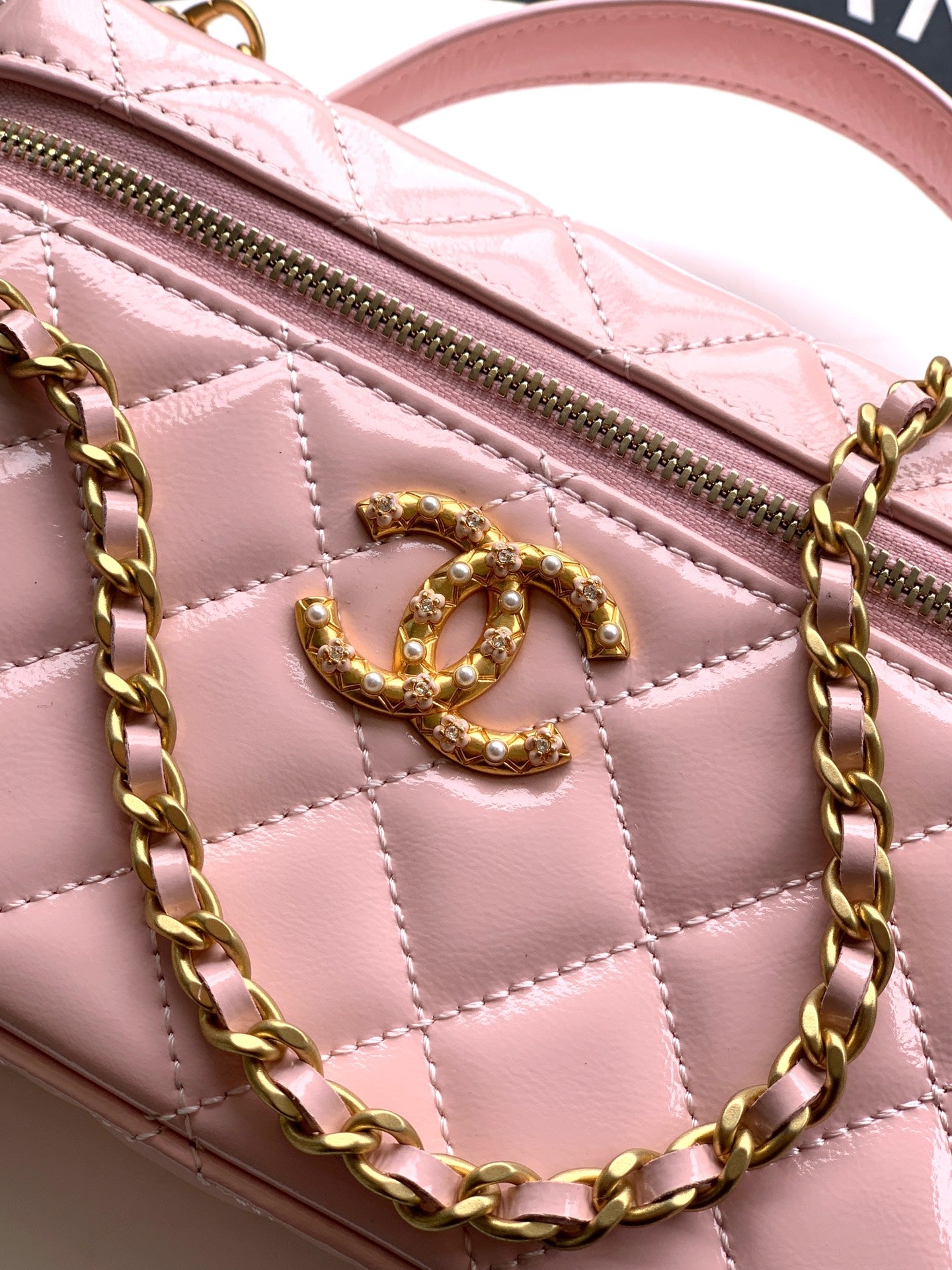 Light pink quilted leather bag close-up of gold-tone CC logo and zipper