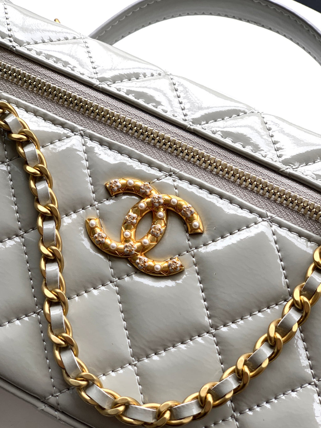 Chanel quilted bag detail, gold-tone CC emblem and zip pull on light silver-gray