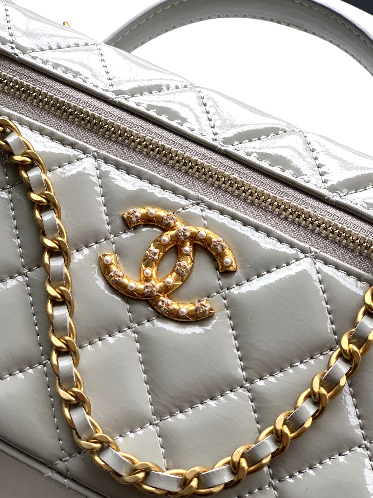 Chanel quilted bag detail, gold-tone CC emblem and zip pull on light silver-gray