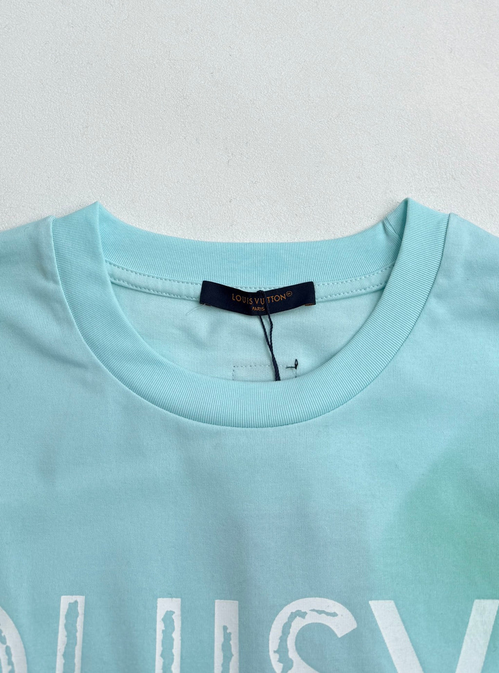 Louis Vuitton T-shirt neckline in light turquoise with brand label at collar.
