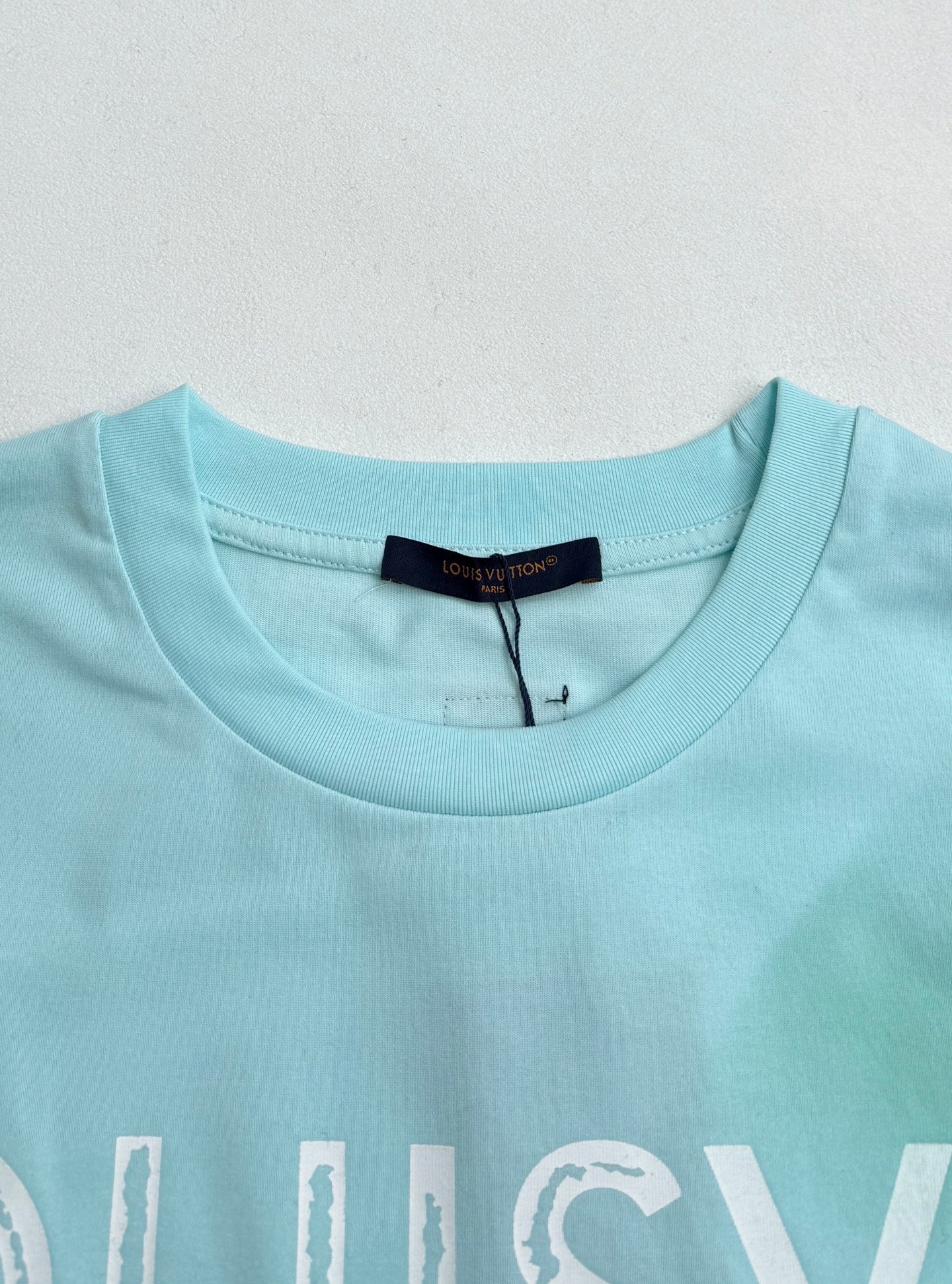Louis Vuitton T-shirt neckline in light turquoise with brand label at collar.