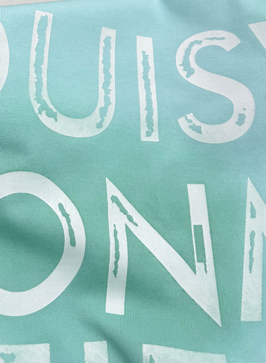 Louis Vuitton front lettering on light turquoise T-shirt, close-up typography.