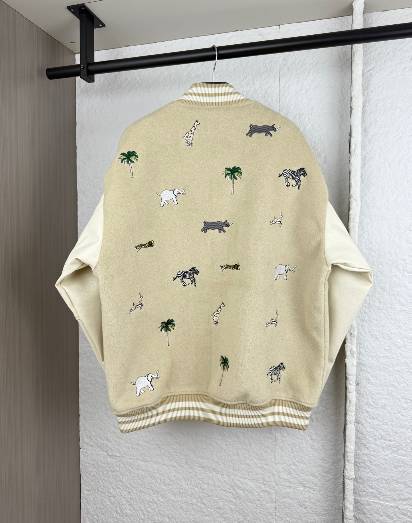 Beige jacket back with scattered animal and palm tree embroidery; ribbed hem and cuffs.
