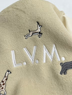 Beige jacket chest detail with embroidered “LV.M” lettering and animal motifs.