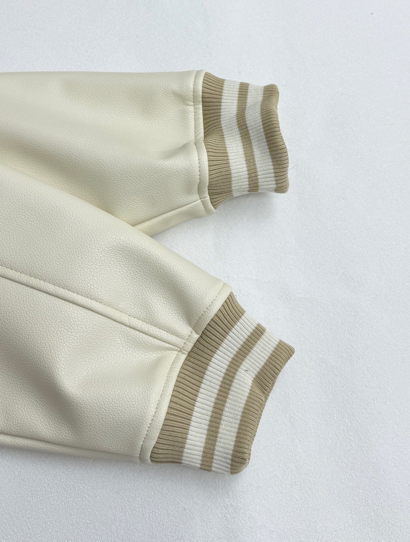 Cream jacket sleeve cuff and hem with striped rib knit trim.