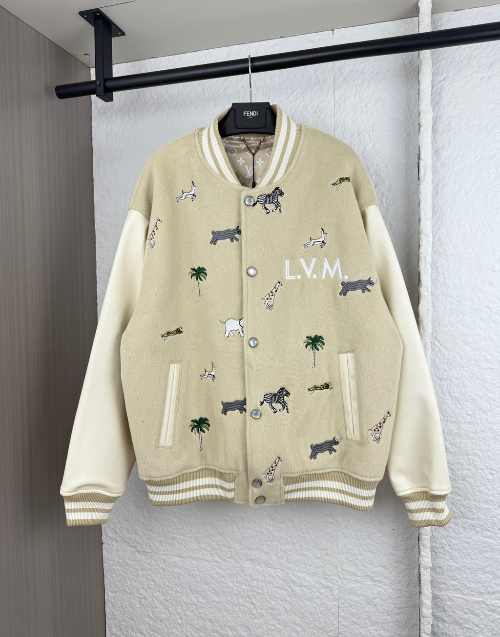 Beige varsity jacket with animal and palm prints, ribbed cuffs, and button front detail.