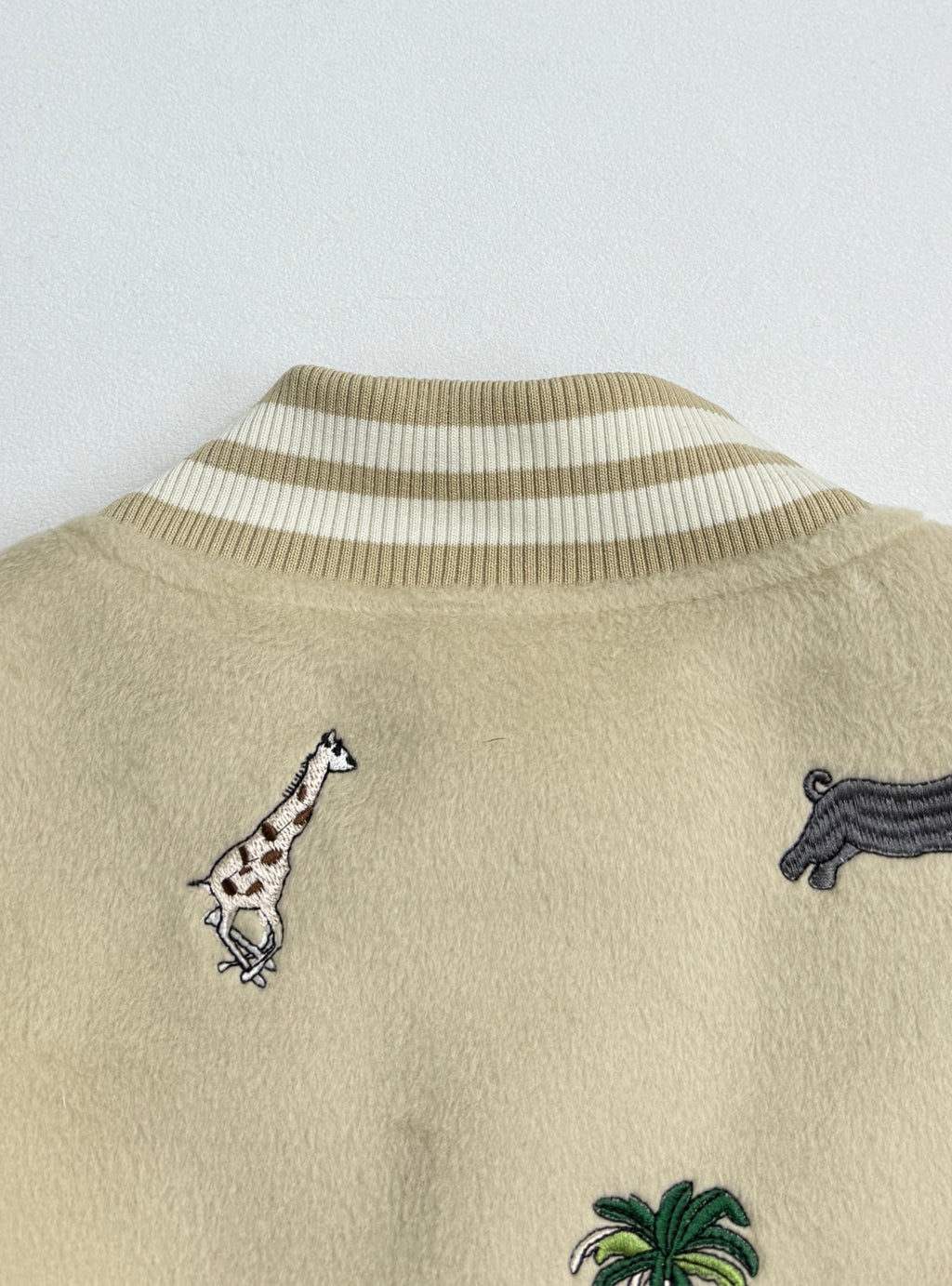 Beige jacket back with striped rib collar and embroidered animal motifs including zebra and dog.
