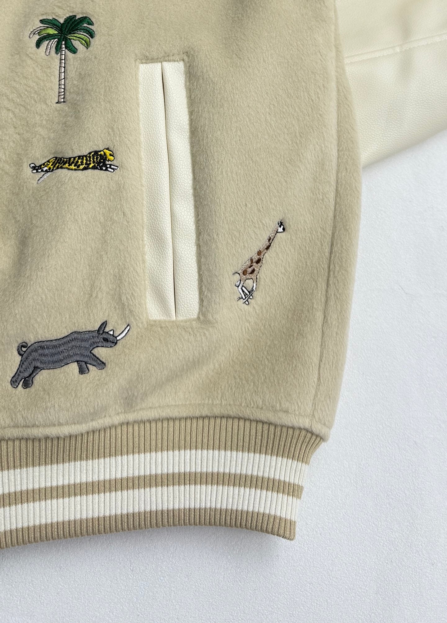 Beige sleeve with animal embroidery and a pocket; striped ribbed cuff and hem trim.
