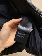 Black puffer vest interior label under hand, PRADA branding tag.