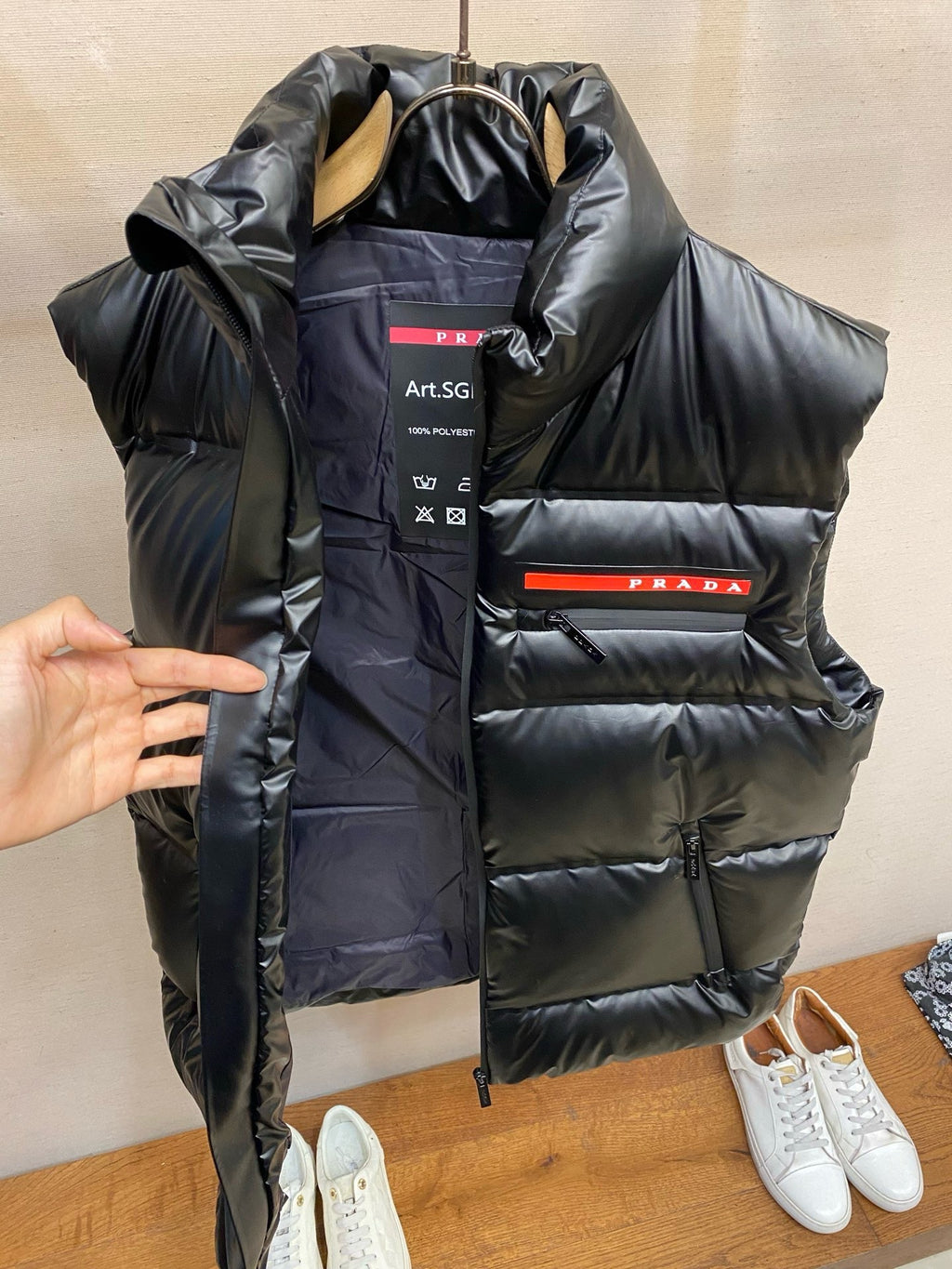 Black long padded vest with PRADA logo band and hood, hanging view.
