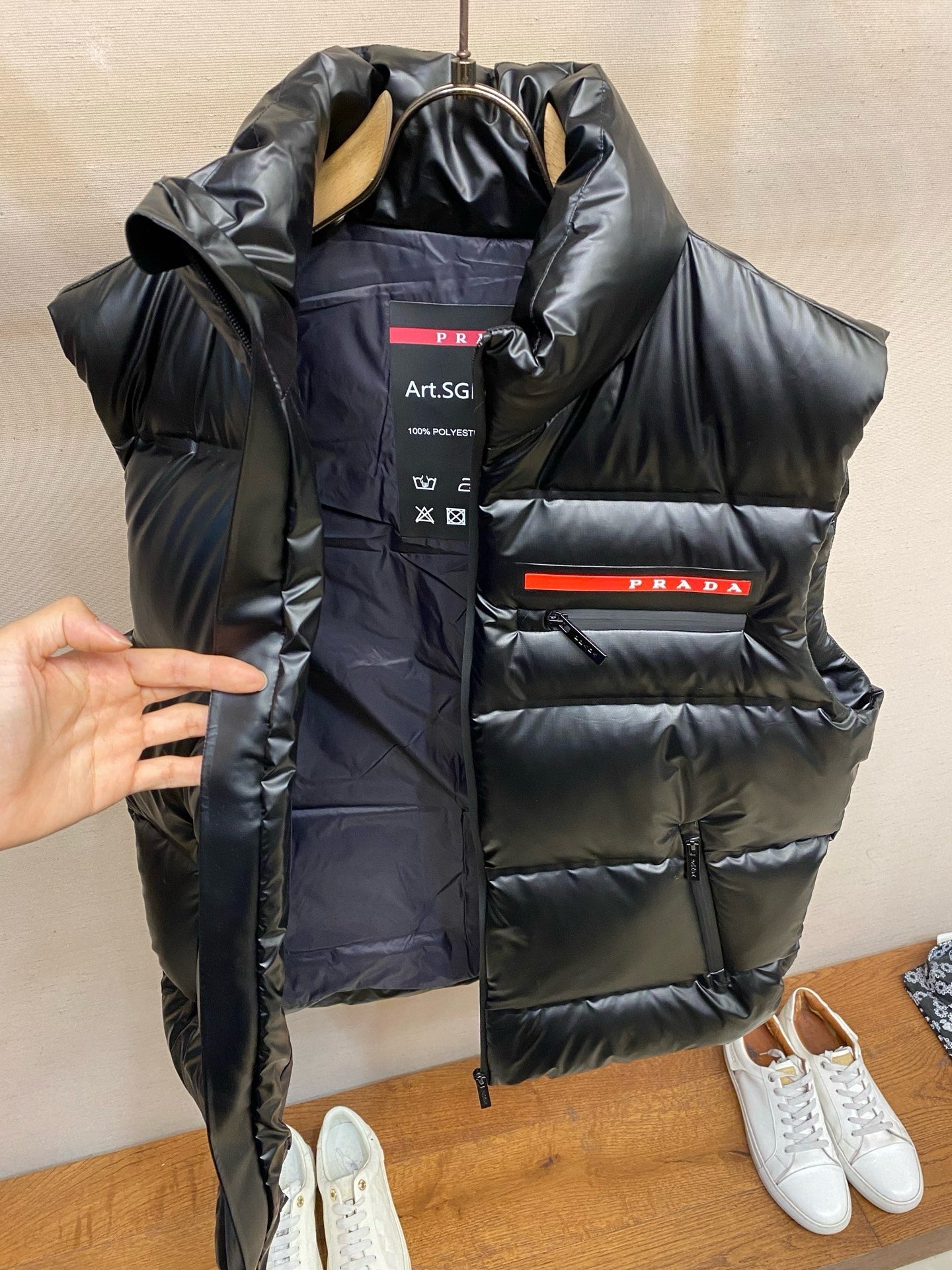 Black long padded vest with PRADA logo band and hood, hanging view.