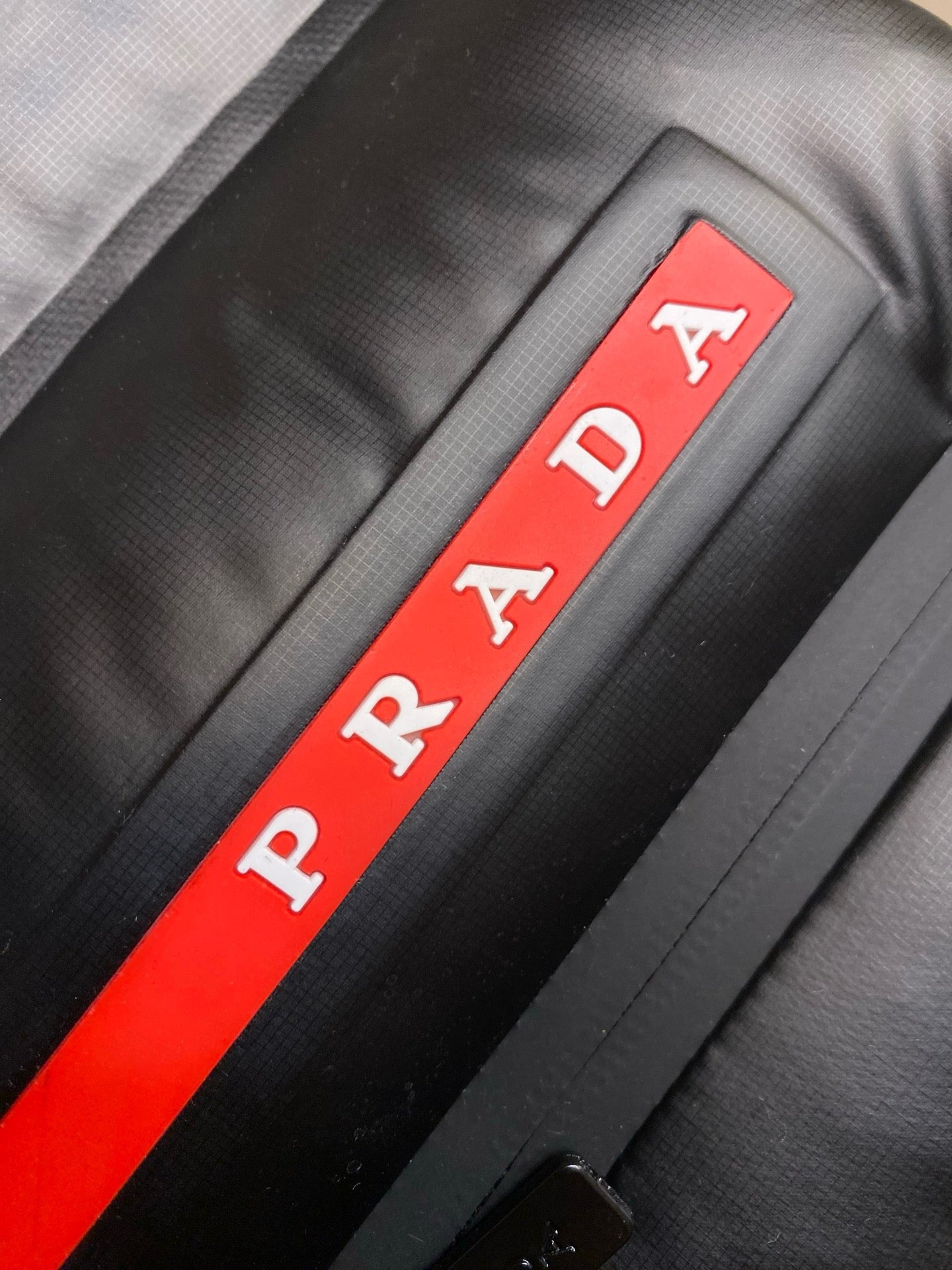 PRADA logo stripe on black fabric, red and white branding.