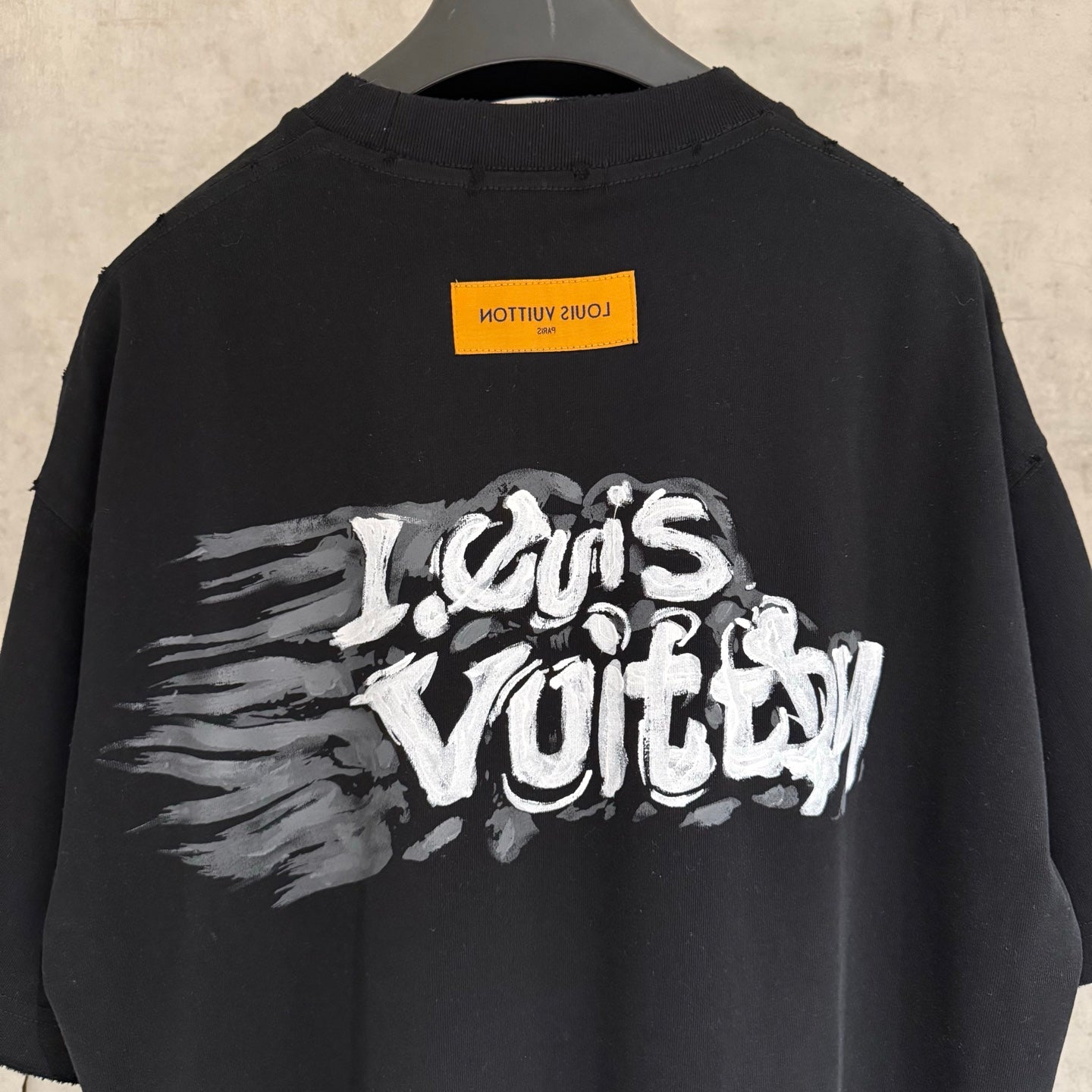 Black T-shirt back with large white graffiti-style logo and yellow label.