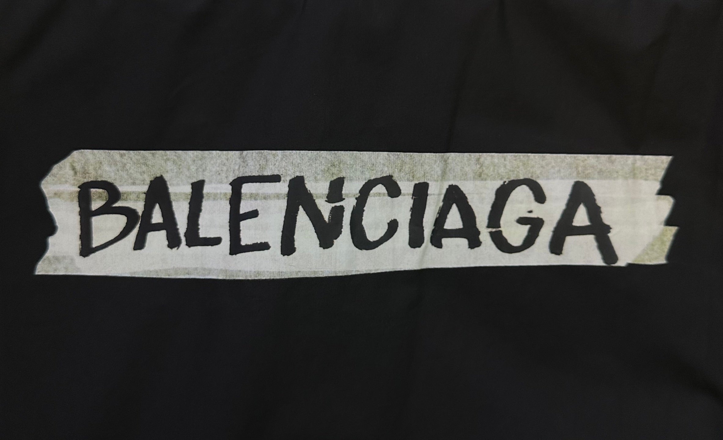 Balenciaga logo patch in white on dark black fabric.