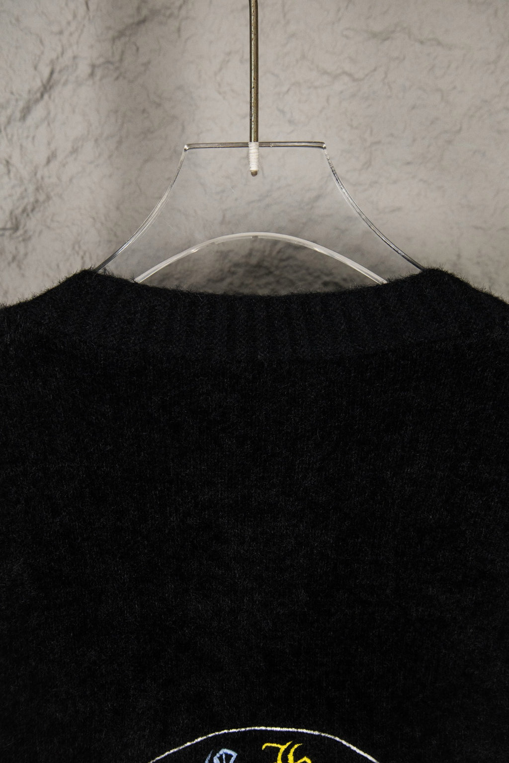 Black cardigan upper back close-up on hanger with partial emblem graphic