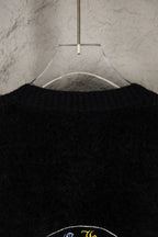 Black cardigan upper back close-up on hanger with partial emblem graphic