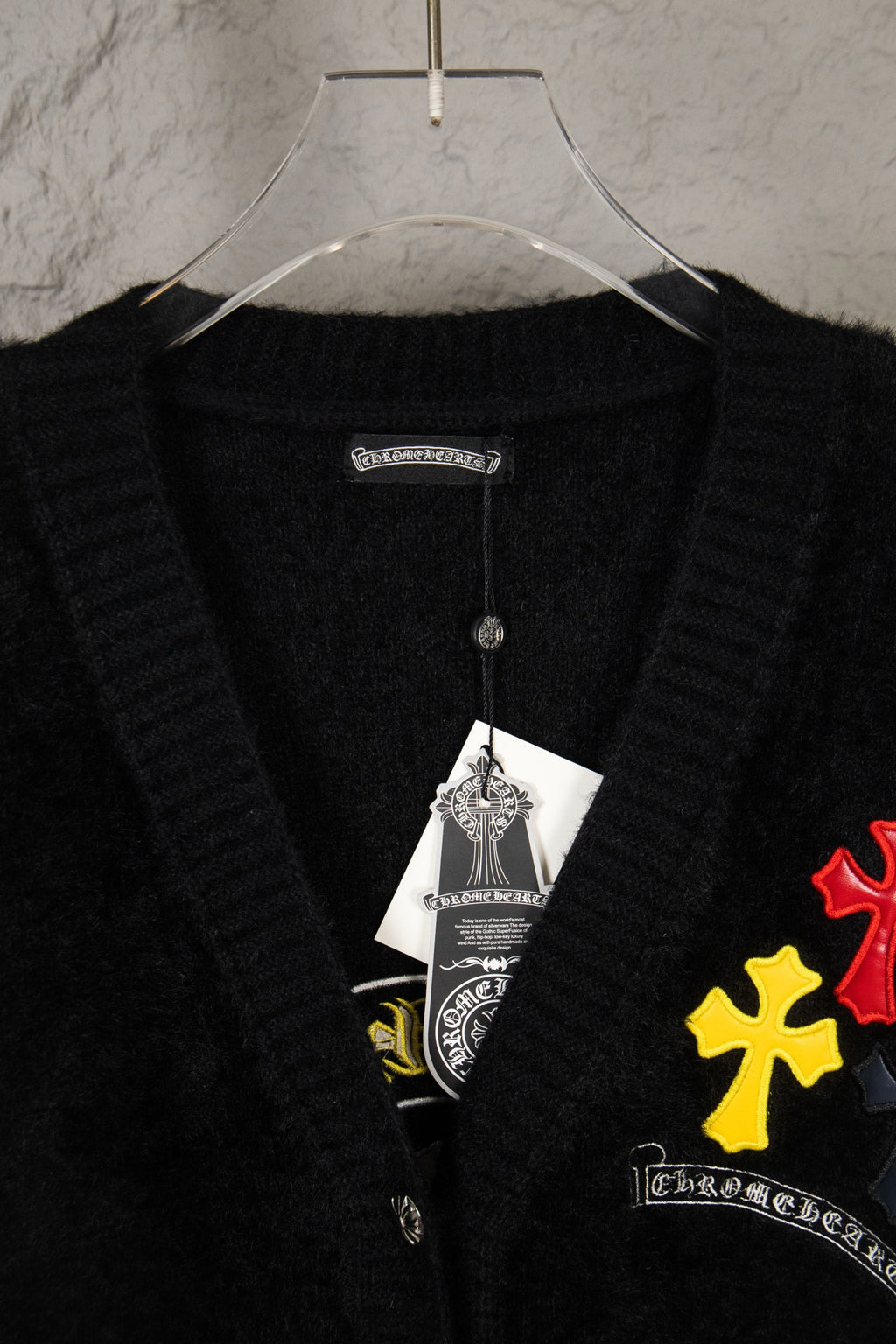 Black cardigan close-up at neckline with inner tag and multicolor chest patch