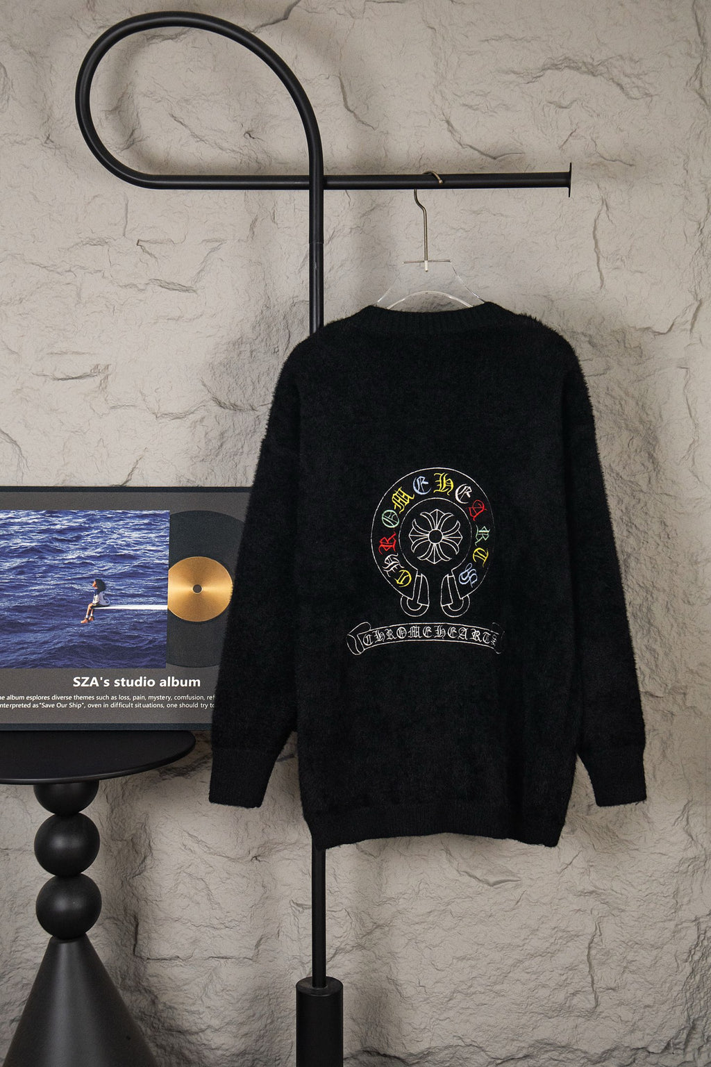 Black cardigan sweater on hanger with large round back emblem graphic