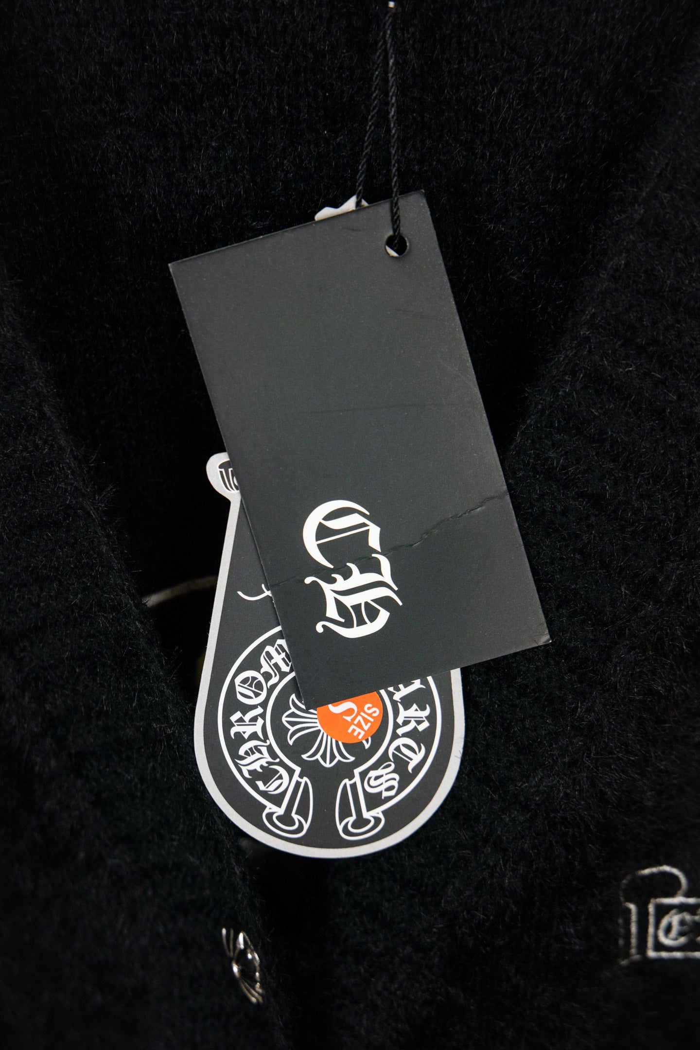 Black cardigan with attached gray hang tag showing white logo symbol